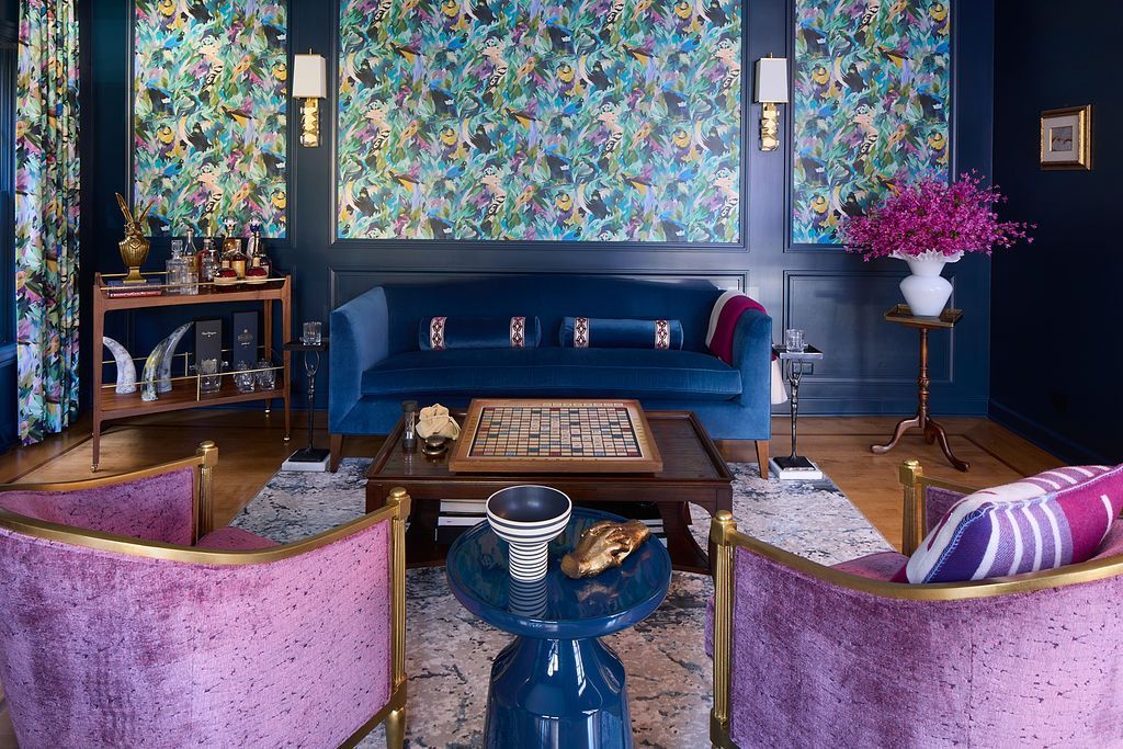 Living room with floral wallpaper, blue sofa, and pink velvet chairs.