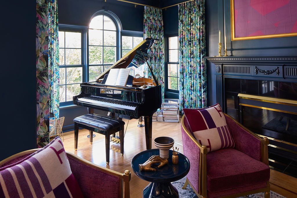 Room with grand piano, velvet chairs, blue walls, patterned curtains, and a fireplace.