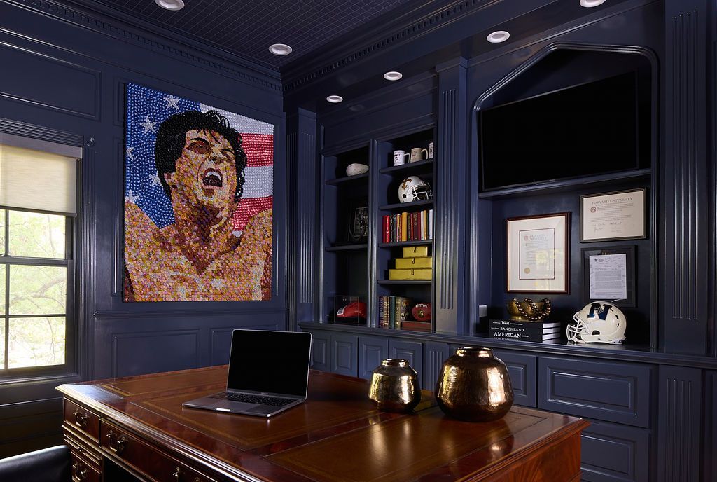 Dark blue home office with desk, bookshelves, and portrait of Sylvester Stallone.