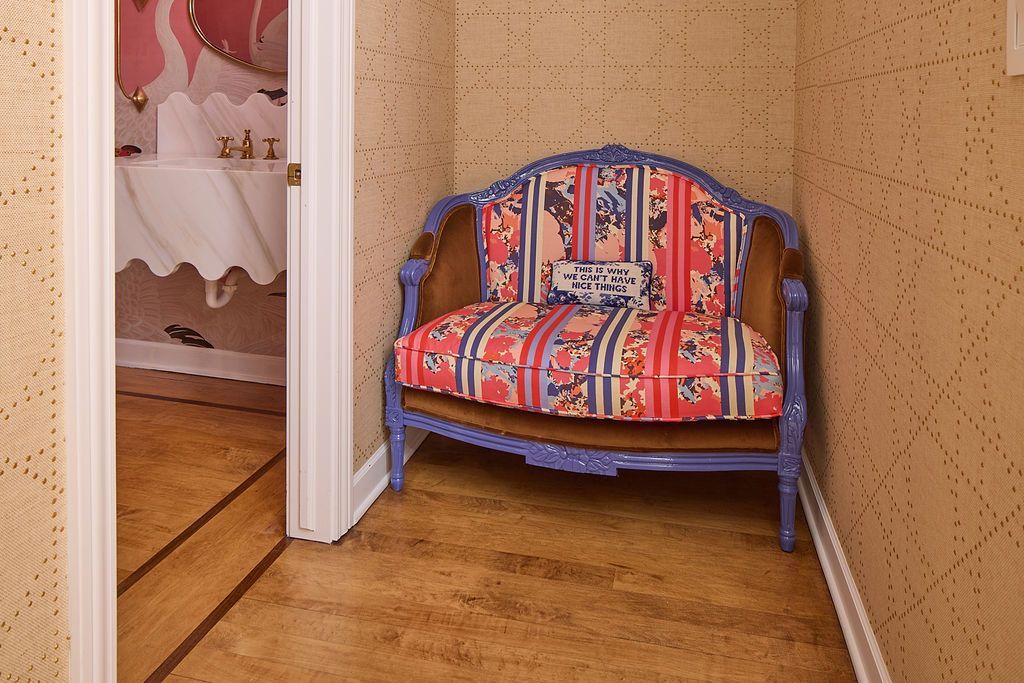 Ornate chair in a hallway; red and blue patterned upholstery, purple frame, beige patterned wallpaper, wooden floor.
