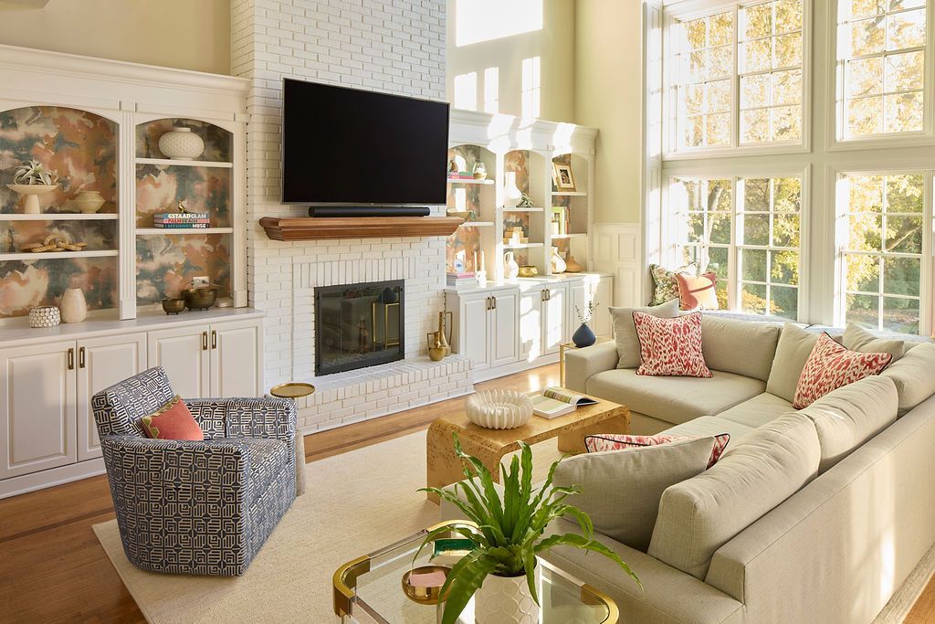 Living room with white brick fireplace, built-in shelves, sectional sofa, and large windows.