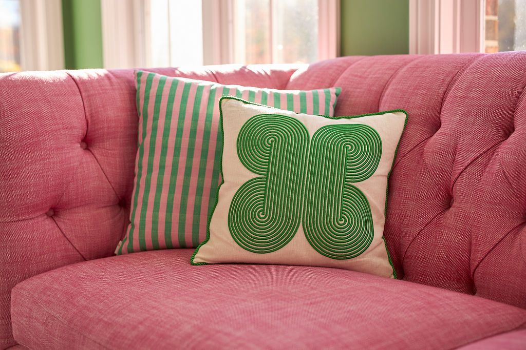 Pink tufted sofa with two green and white patterned pillows.