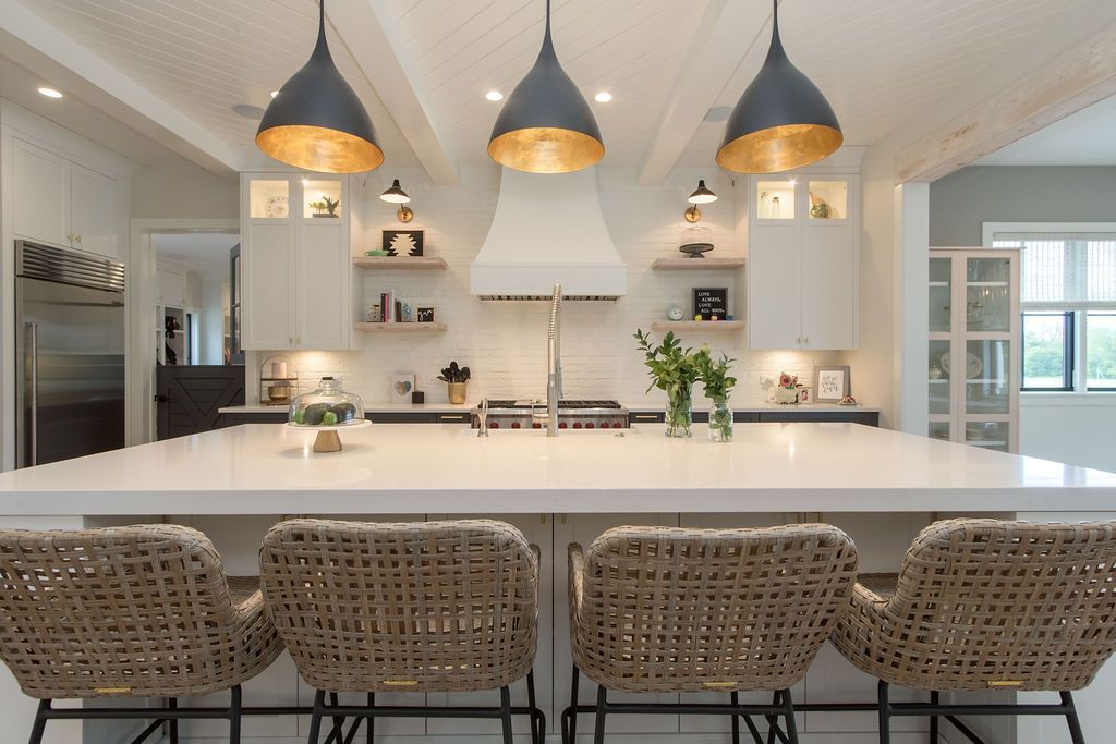 Kitchen with white island, black pendant lights, woven bar stools, and white cabinetry.