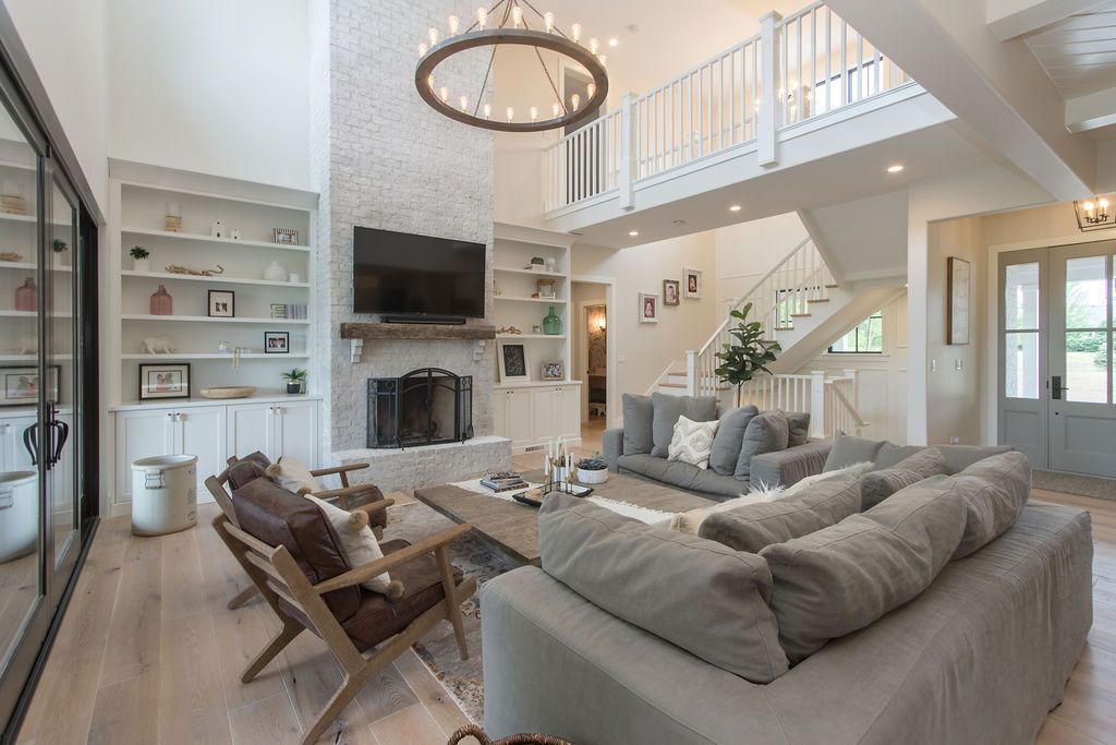 Spacious living room with high ceilings, fireplace, and two-story balcony; neutral color palette and modern decor.