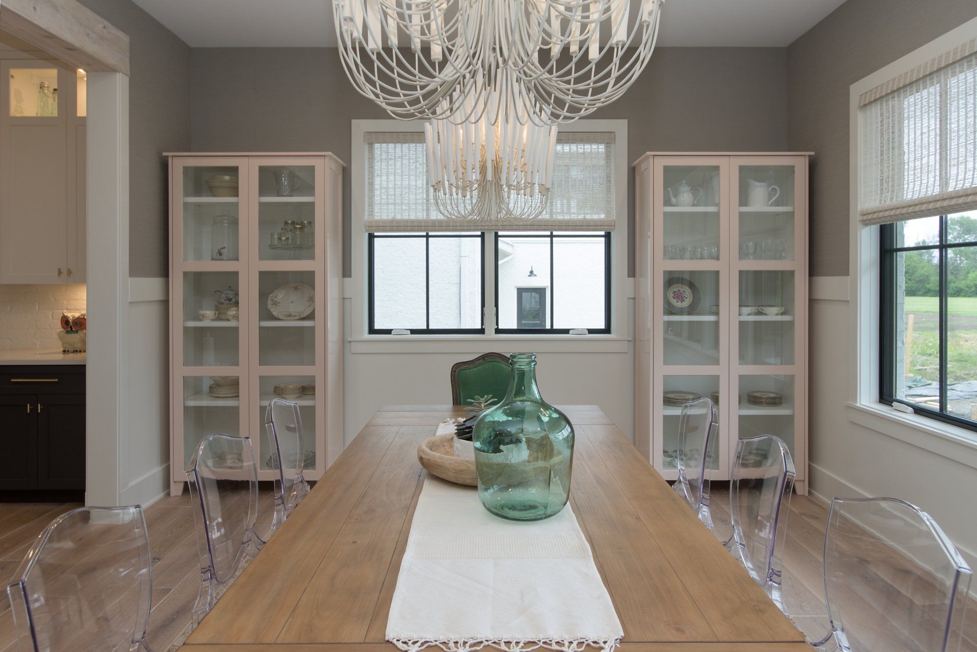 A dining room with a long wooden table and clear chairs and a chandelier.