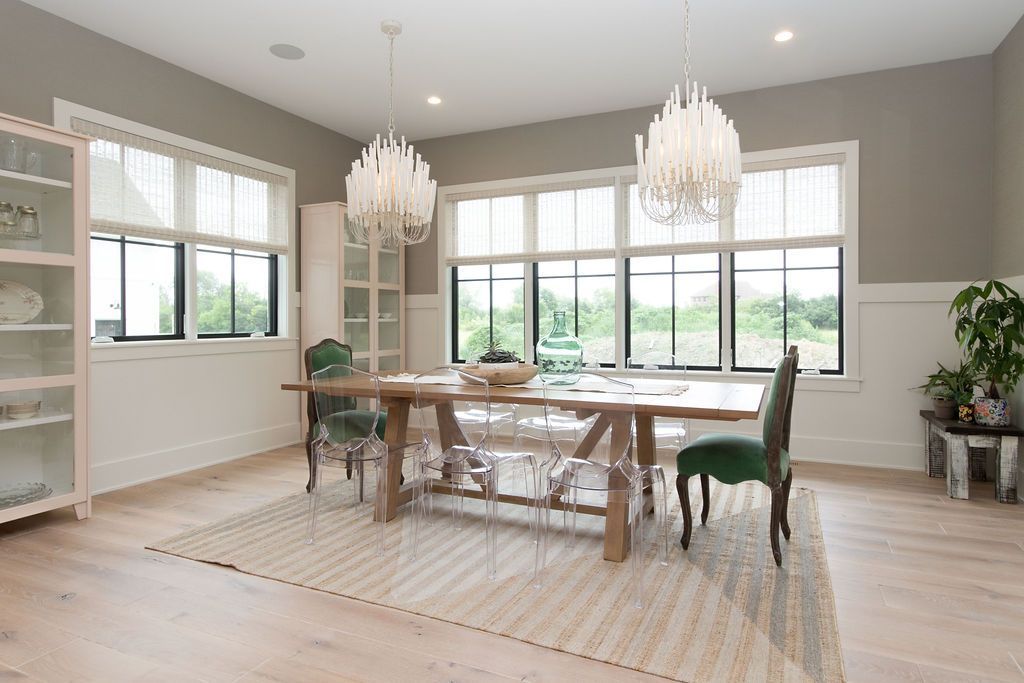 Dining room with wooden table, green chairs, crystal chandeliers, and large windows.