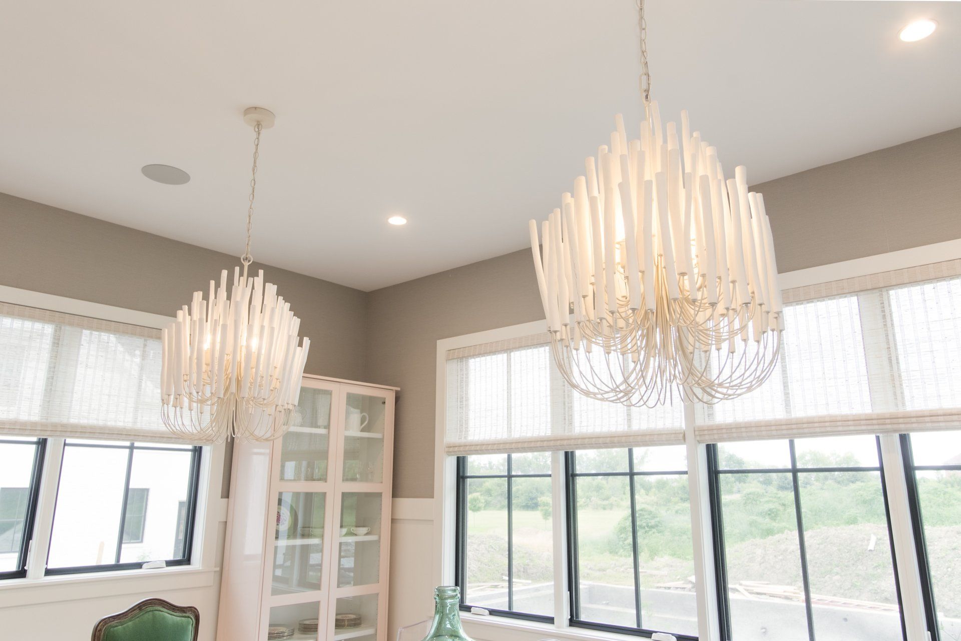 Two chandeliers are hanging from the ceiling in a room with lots of windows.