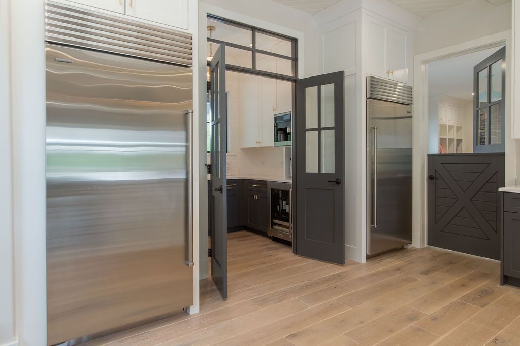 Kitchen with stainless steel refrigerator, pantry, and dark gray doors, light wood floors, and white walls.