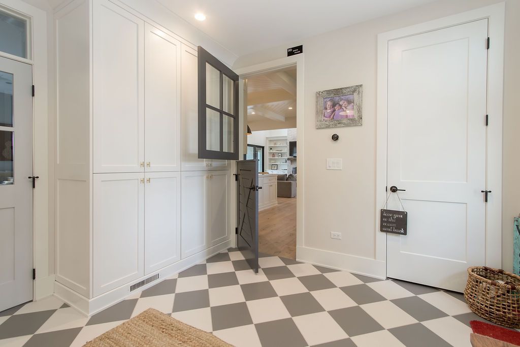 Hallway with checkered floor, built-in white cabinets, open gray Dutch door, and a white door on the right.