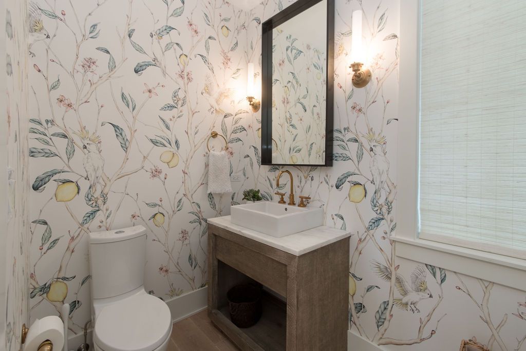 Powder room with floral wallpaper, wooden vanity, rectangular mirror, and sconces.