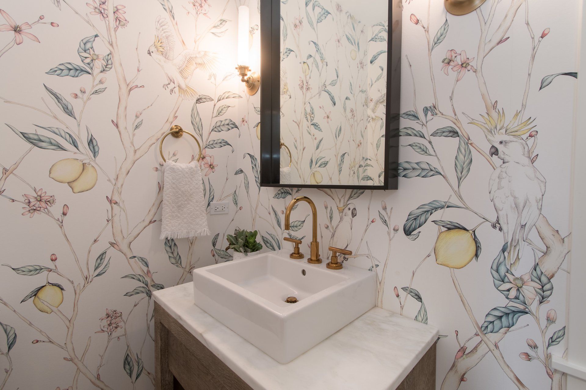 A bathroom with a sink , mirror , and floral wallpaper.