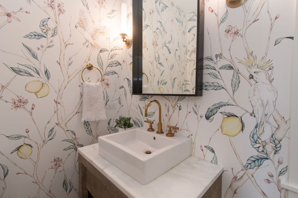 Powder room with floral wallpaper, gold faucet, square sink, and mirror.