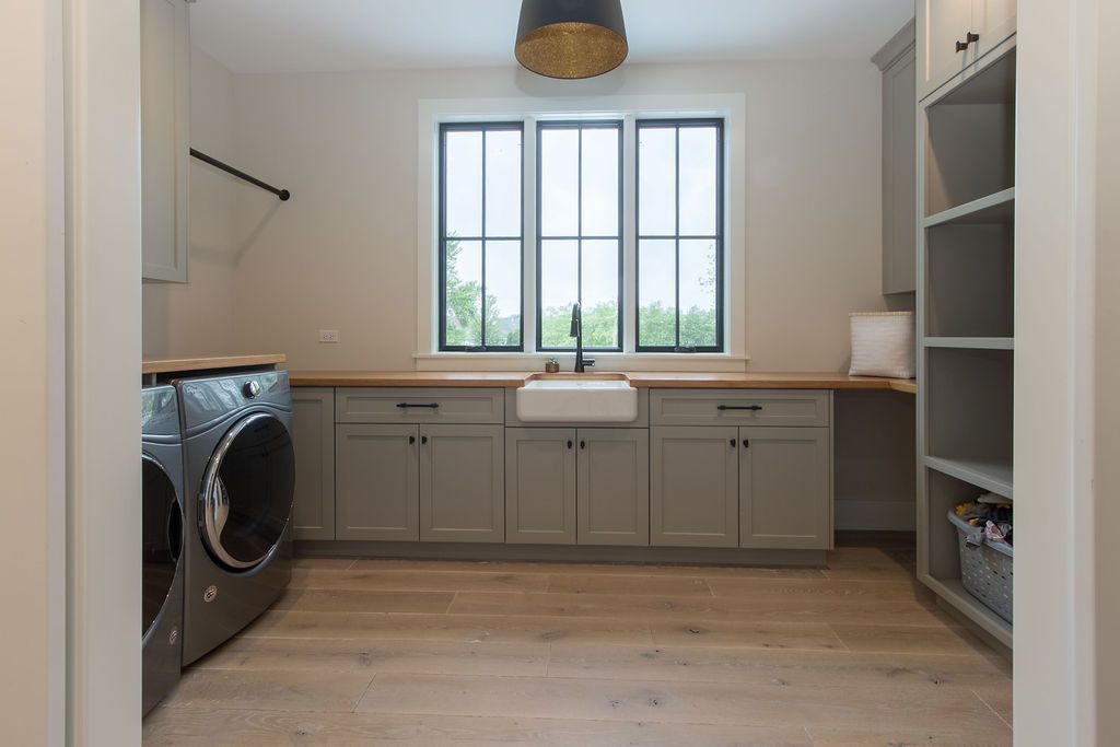 Laundry room with gray cabinets, wooden countertop, and large window.
