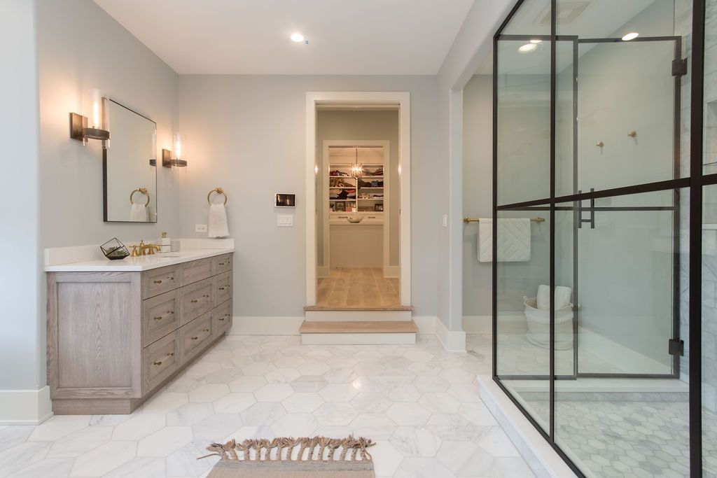 Spacious bathroom with marble floors, a glass shower, vanity, and a doorway leading to another room.