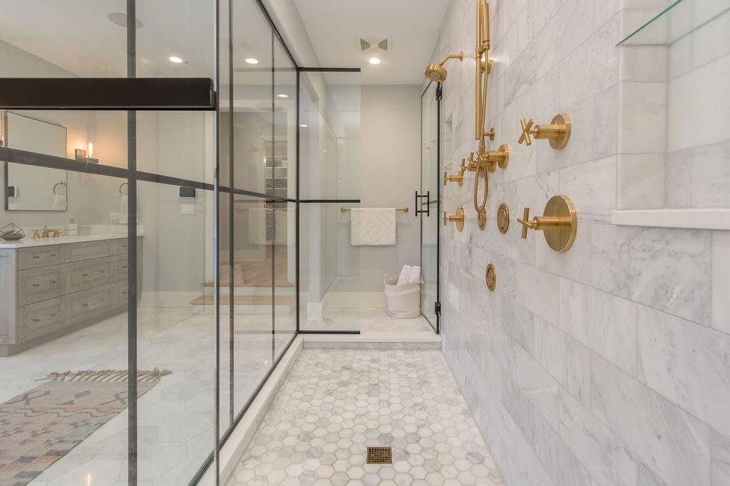 Luxurious modern bathroom with marble tile and gold fixtures; glass shower.
