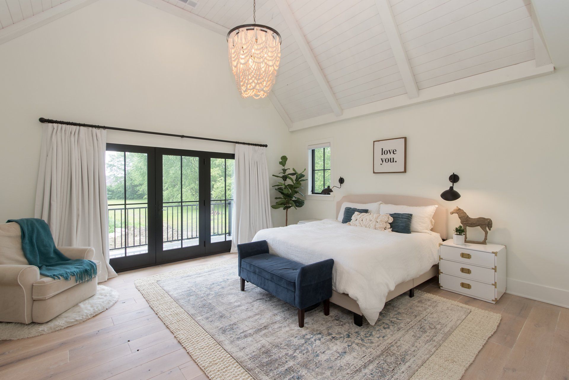 A bedroom with a bed , chair , nightstand , rug and chandelier.