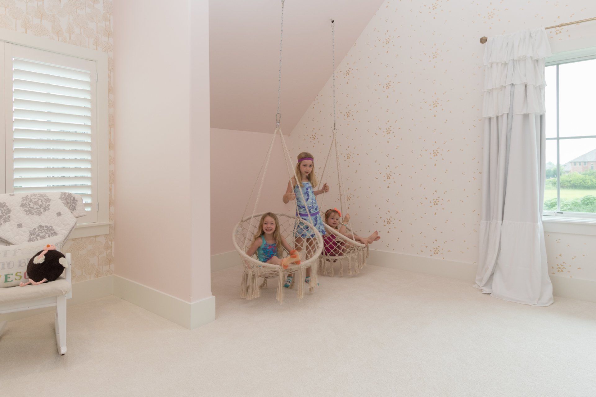Three little girls are sitting in hanging chairs in a room.