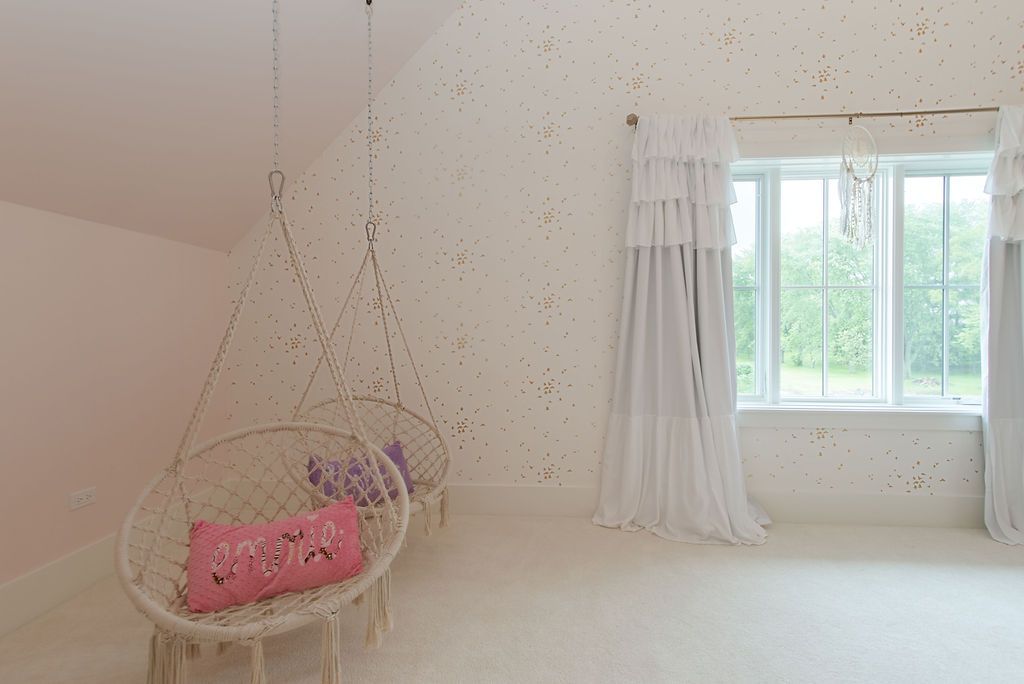 A light-filled room with hanging macrame chairs, a window with curtains, and a textured wall.