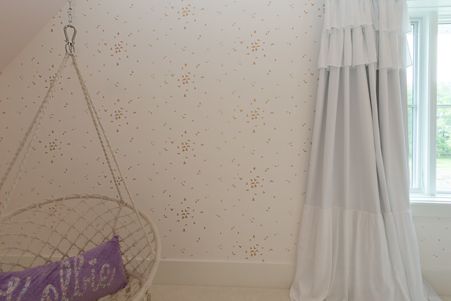 There is a hanging chair in the room with a purple pillow.