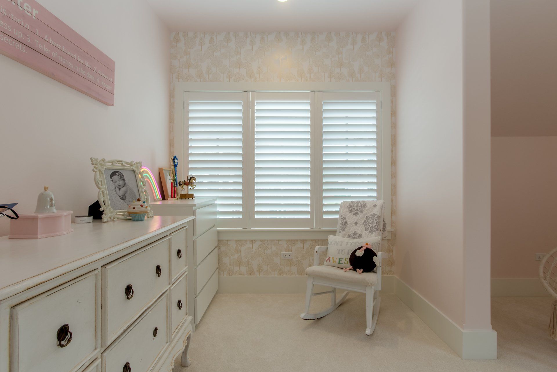 A bedroom with a rocking chair , dresser , and window.