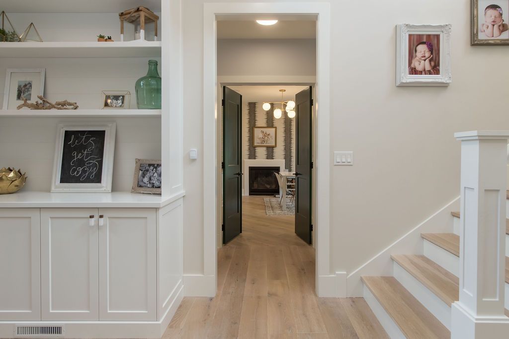 Hallway with light wood floors, built-in shelving, staircase, and open doors leading to a fireplace.