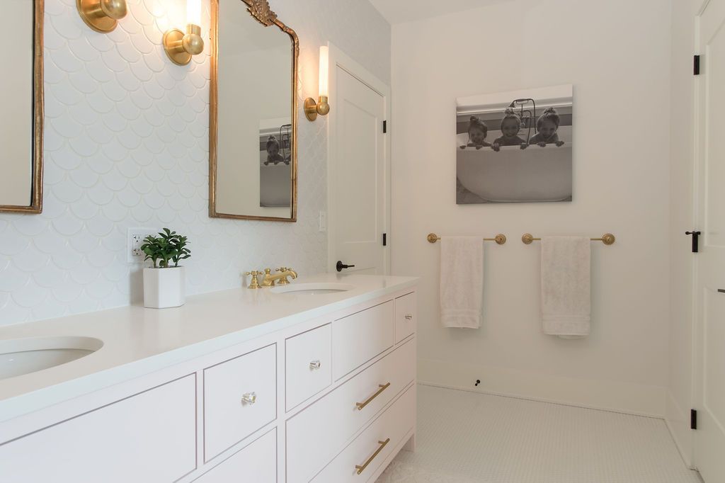 White bathroom with light pink vanity, gold accents, and white tile floor.