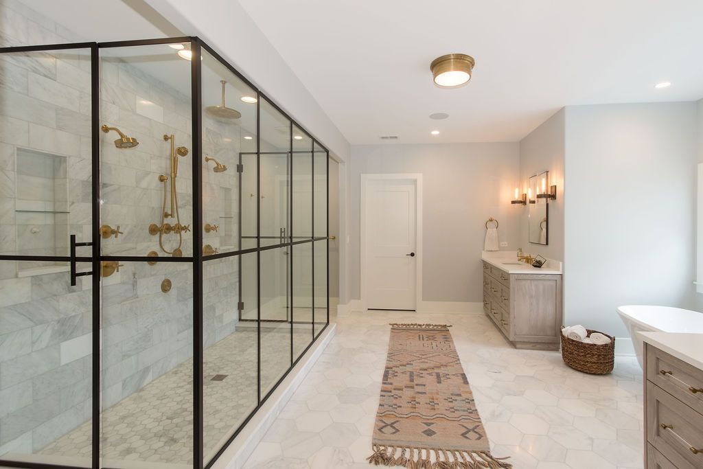 Luxurious bathroom with large glass shower enclosure, marble tile, and neutral color scheme.