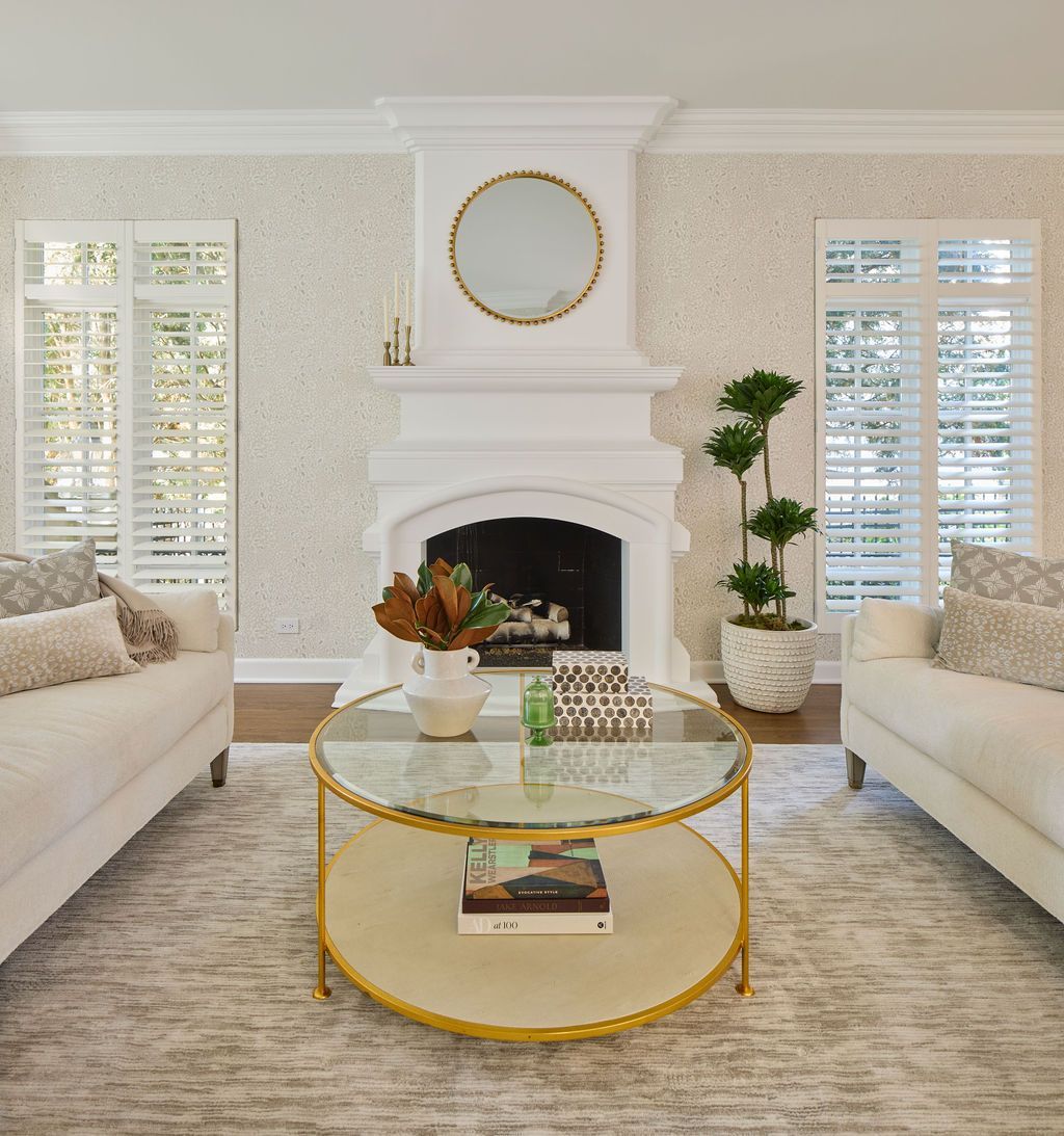 Living room with white sofas, fireplace, gold coffee table, and patterned wallpaper.