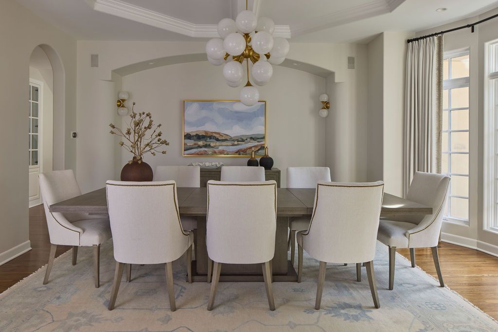Elegant dining room with a long wooden table, white chairs, and a chandelier.