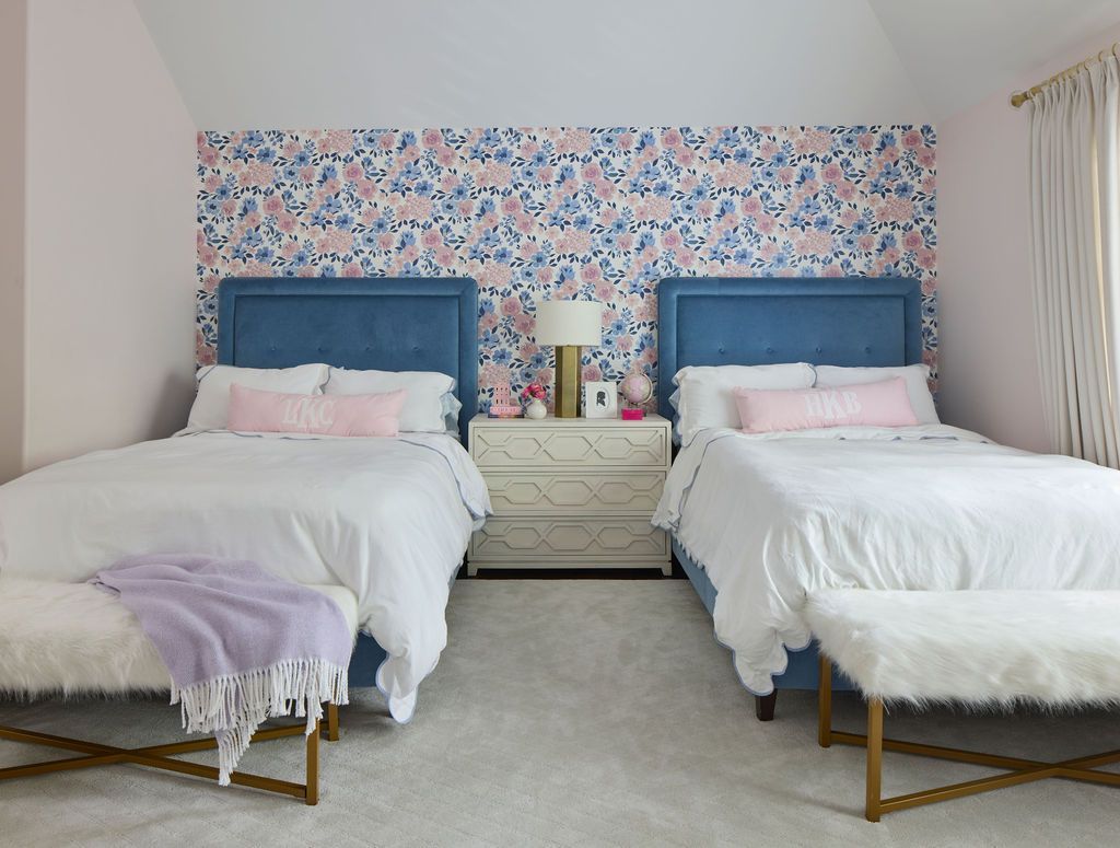 Two twin beds with blue headboards face each other in a bedroom with floral wallpaper.