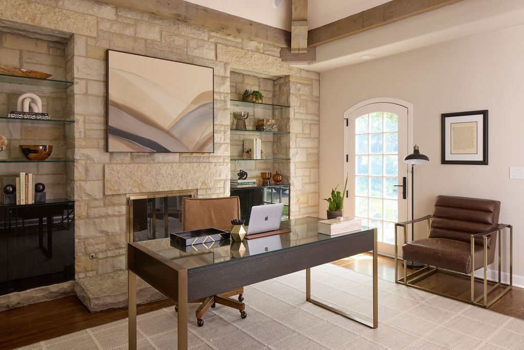 Home office with stone fireplace, glass desk, leather chair, and art.