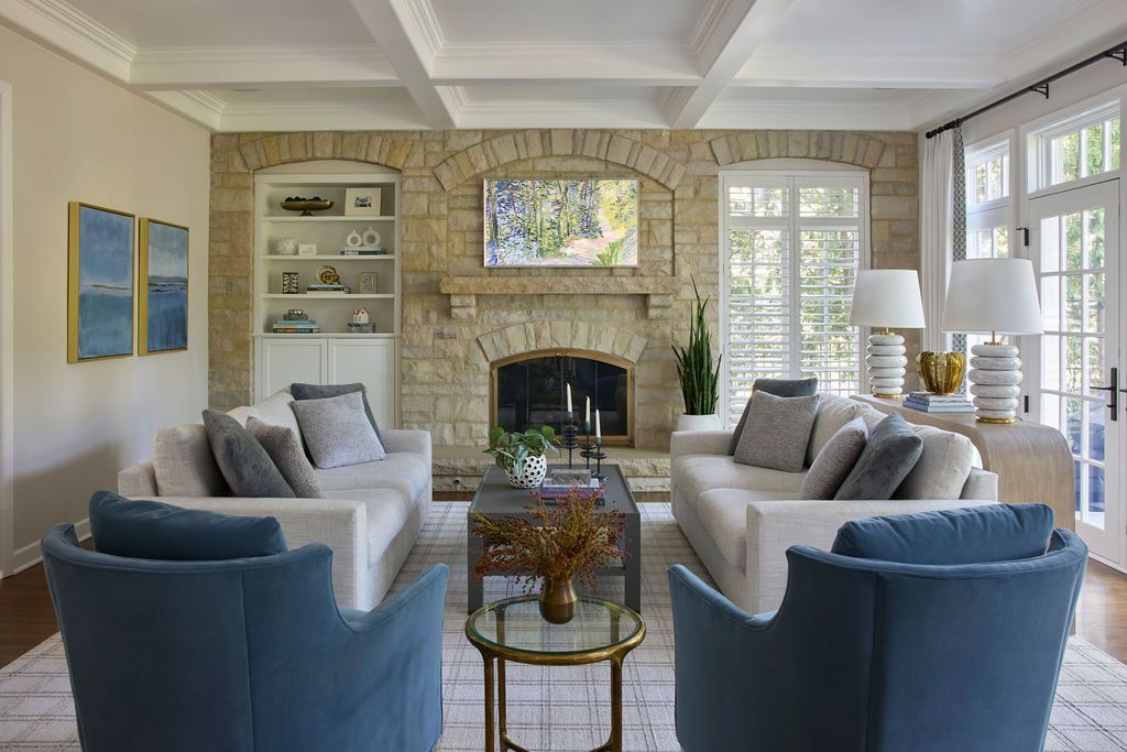 Living room with stone fireplace, sofas, blue chairs, and French doors.