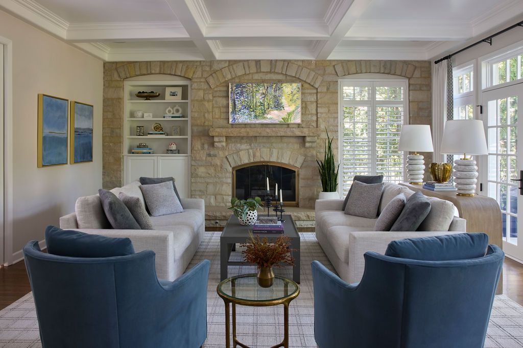 Living room with stone fireplace, sofas, blue armchairs, and a rug.