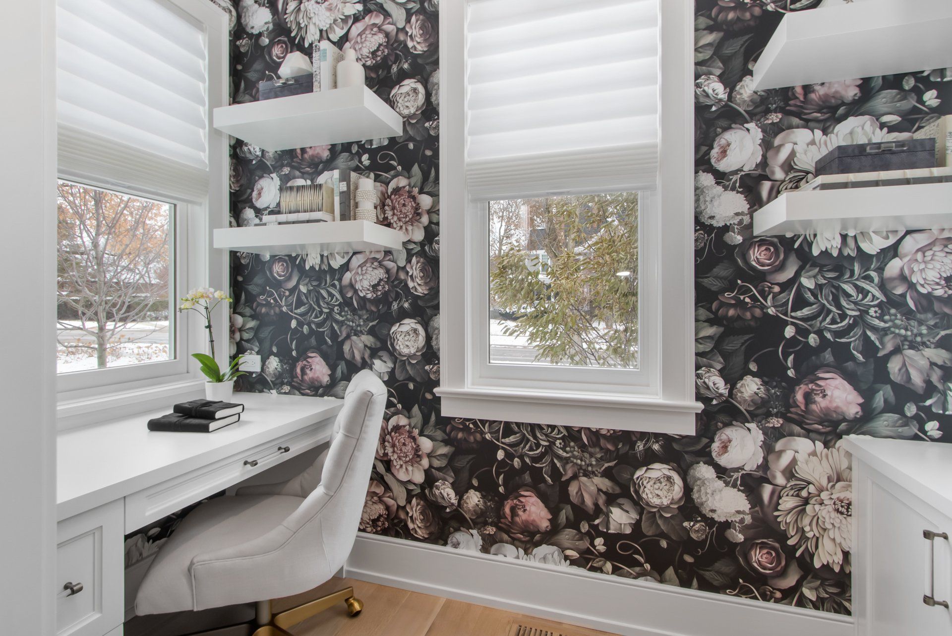 A home office with a desk and chair and floral wallpaper on the wall.
