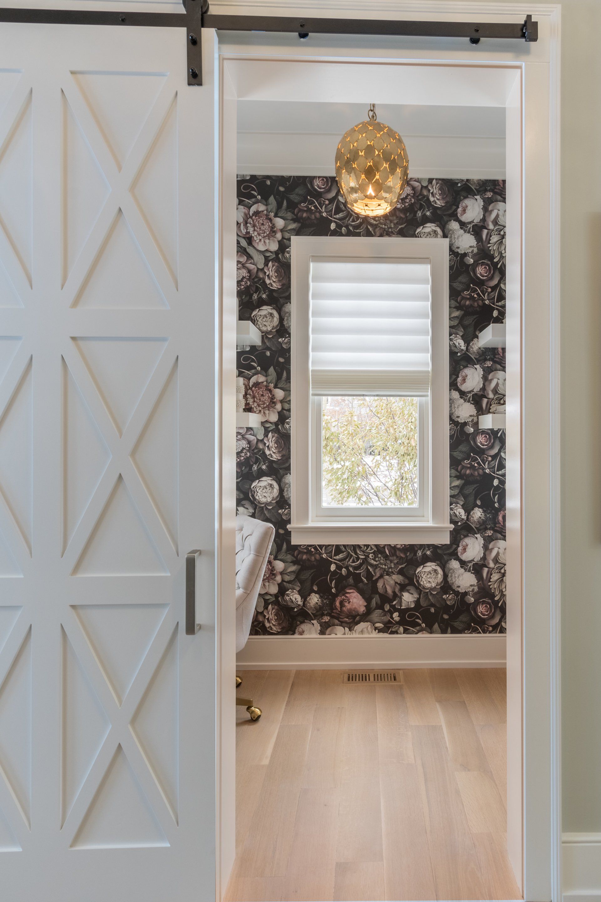 A bathroom with a sliding barn door and floral wallpaper.