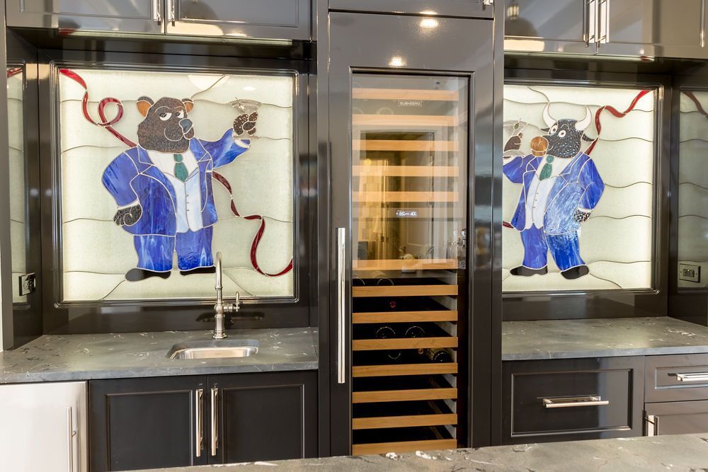 Bar with wine fridge, stained glass art of a bear in suit, holding wine, dark cabinets, gray countertop.