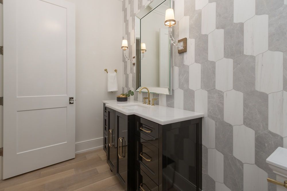 Bathroom with black vanity, gold fixtures, patterned gray and white wall, and a white door.