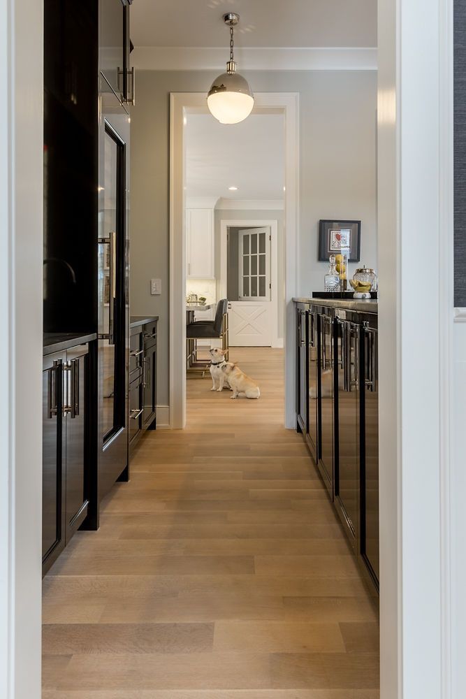 Narrow hallway with wood floors, dark cabinets, and white doorway leading to a brighter room.