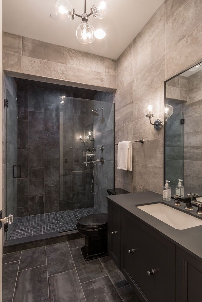 Modern bathroom with dark gray tile walls, walk-in shower, black vanity, and black toilet.