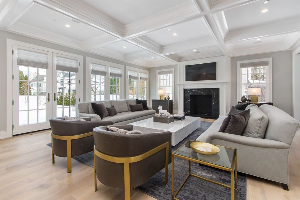 Living room with gray sofas, gold chairs, fireplace, and large windows with snow outside.