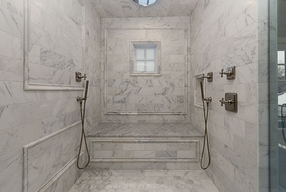 Marble-tiled shower with a bench. Two handheld showerheads, a small window.