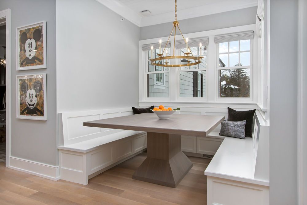 Breakfast nook with a built-in bench and a square table. Windows and a gold chandelier provide light.