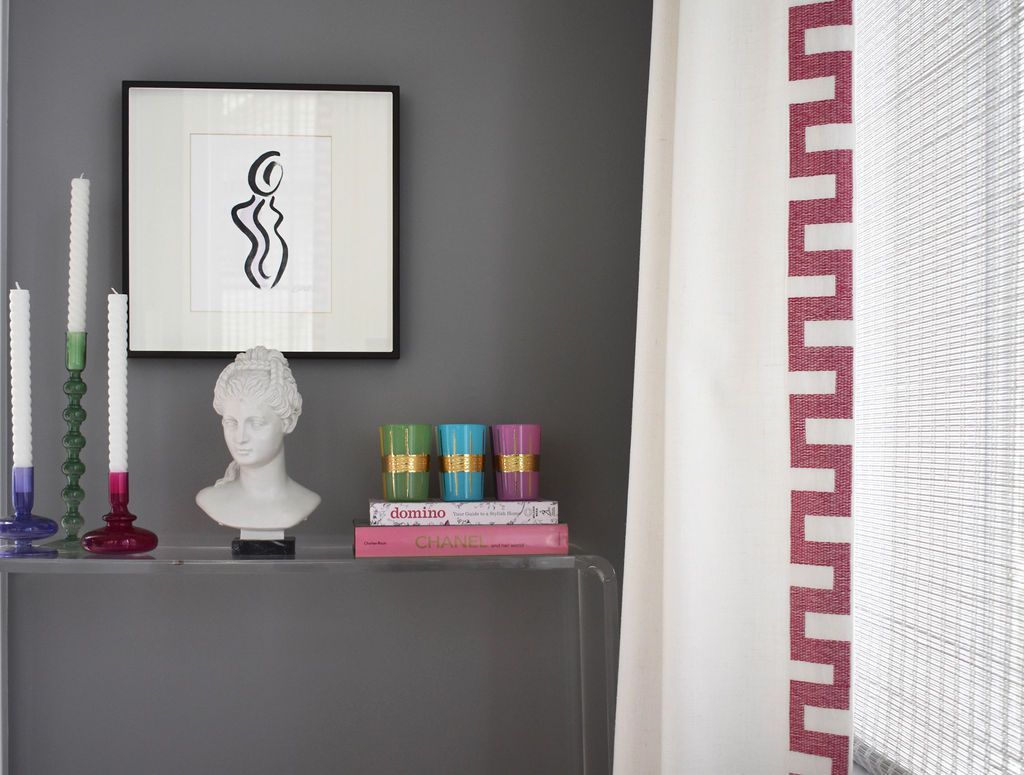 Gray wall with art, candles, bust, books, and curtains with patterned border.