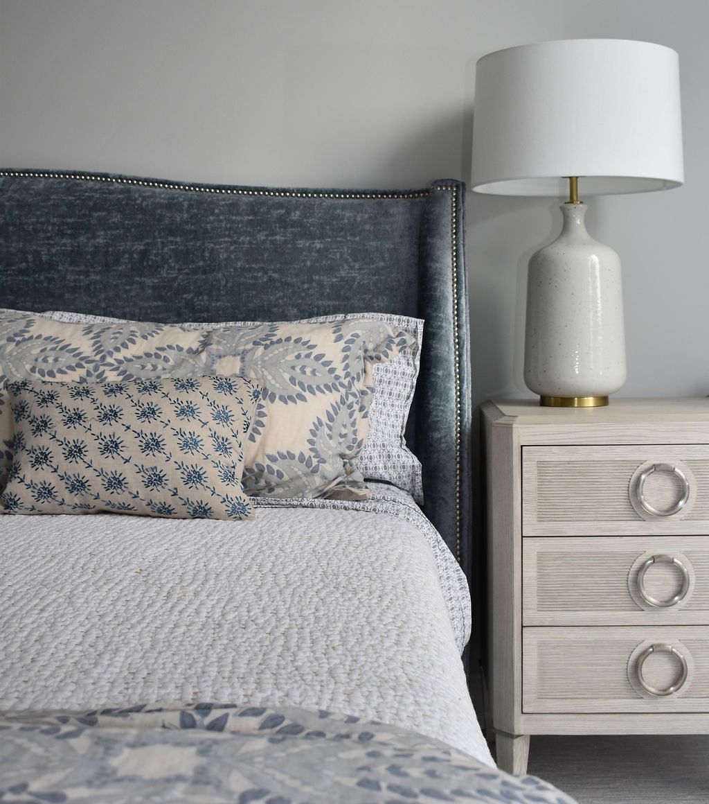 Bed with blue velvet headboard, floral pillows, white bedding, and nightstand with lamp.