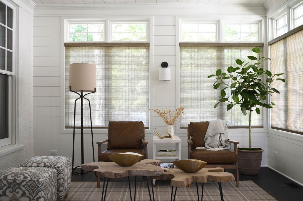 Sunroom with white walls, brown leather chairs, tree-trunk coffee tables, and woven shades.