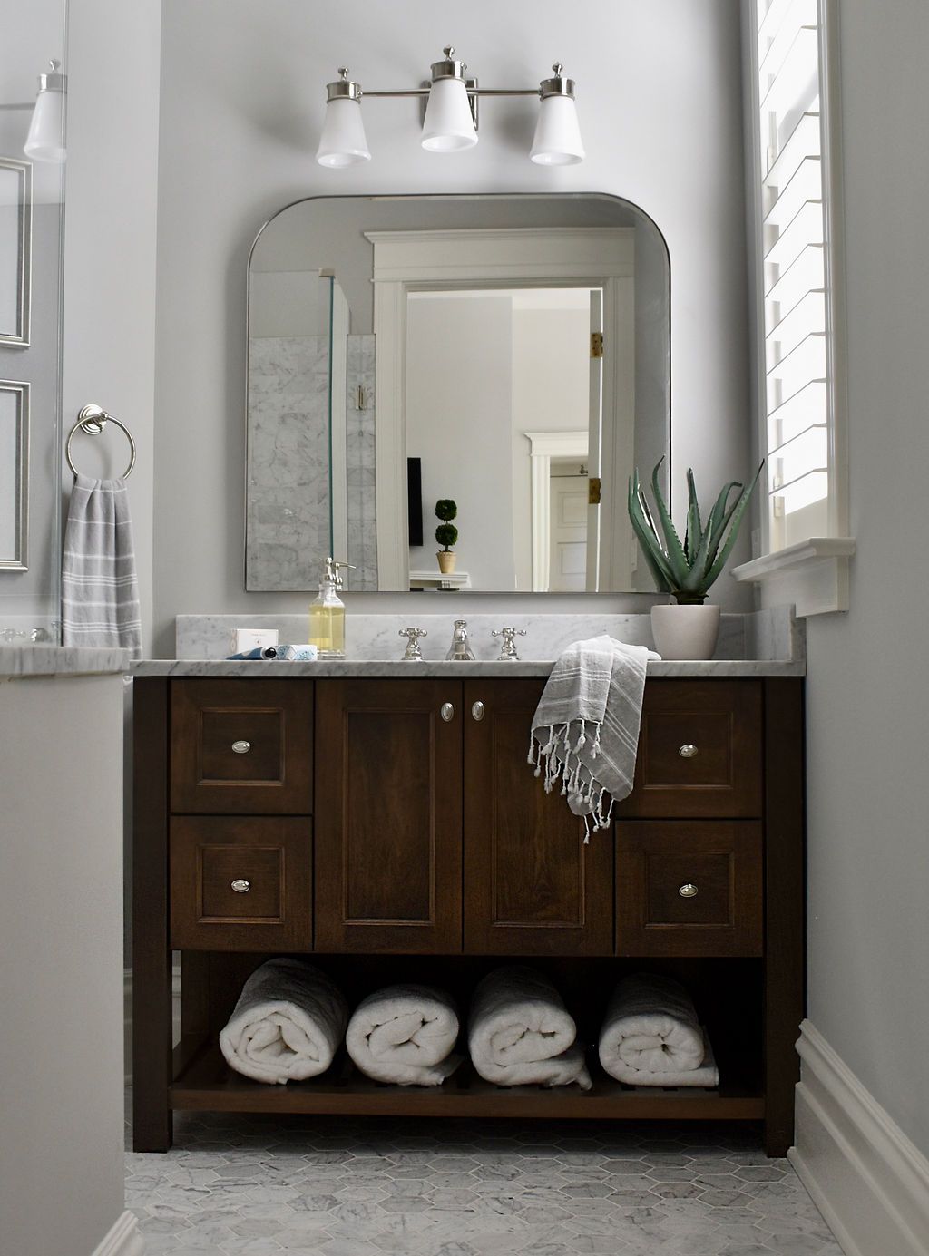 Bathroom vanity with a dark wood cabinet, marble countertop, and arched mirror.