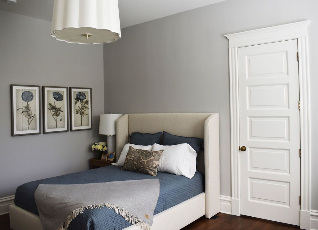 Bedroom with gray walls, bed with blue bedding, framed art, and a white door.