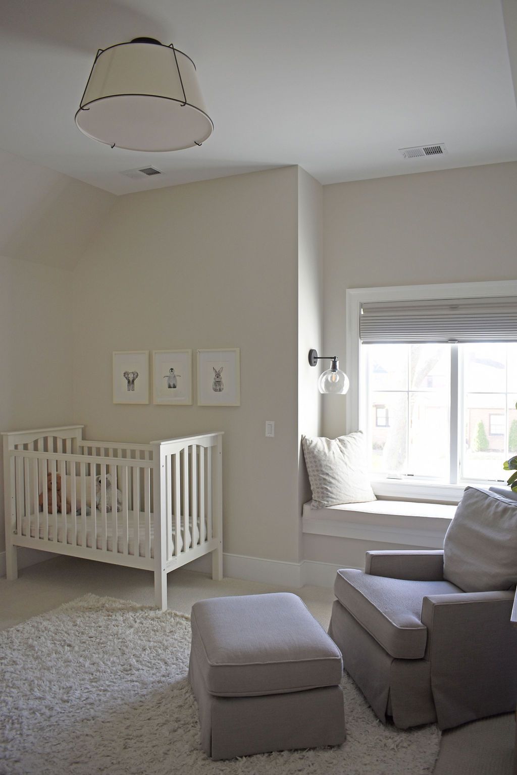 Neutral nursery with white crib, gray armchair, window seat, and rug.