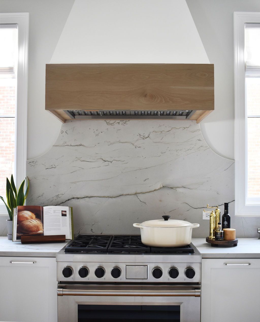 Kitchen with white cabinets, stainless steel stove, wooden range hood, and marble backsplash.