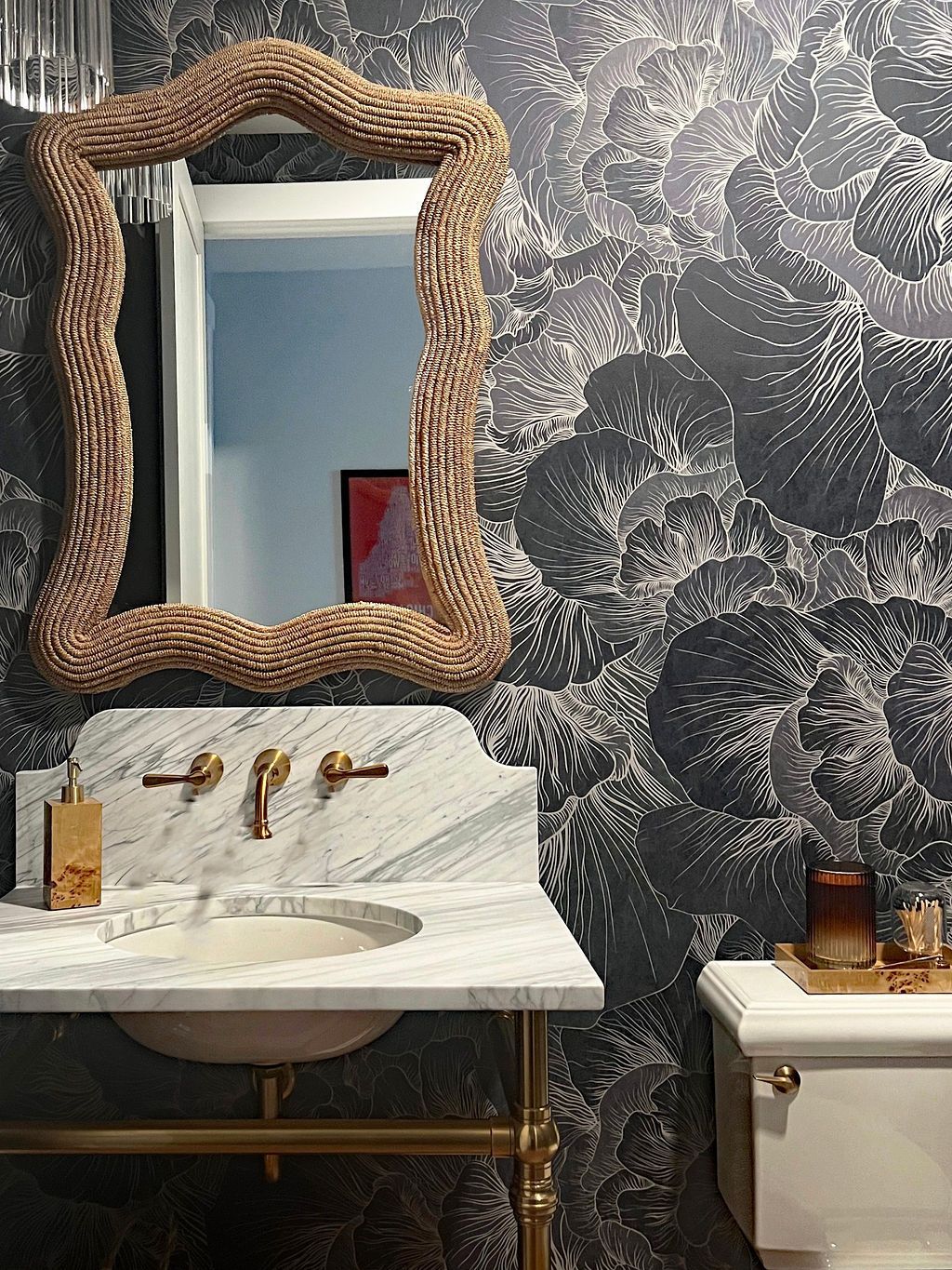 Bathroom with a wavy, textured mirror frame, marble sink, and patterned wallpaper.